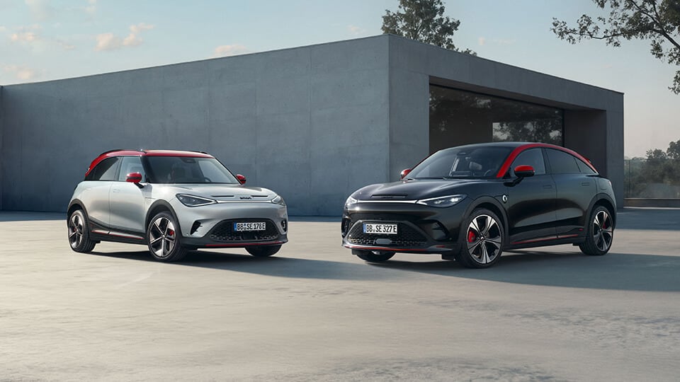 Two smart cars, one silver and one black with red accents, parked near a minimalist concrete building on a clear day